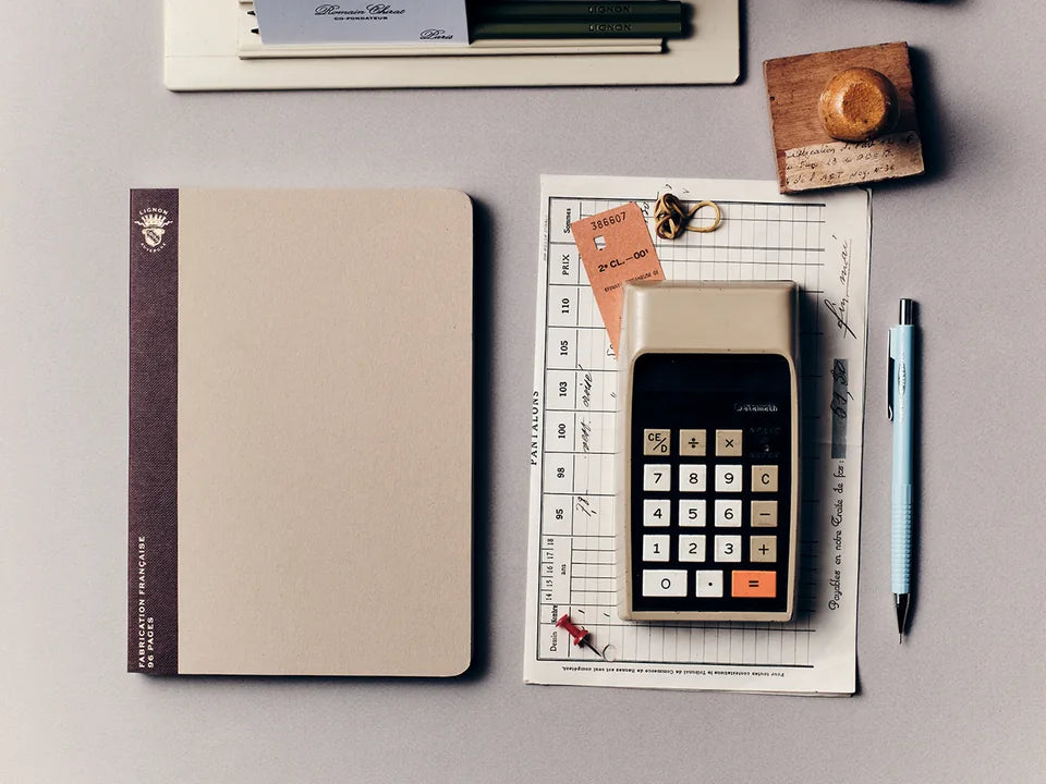 Cahier Lignon beige sur un bureau, avec des papiers anciens et une calculatrice.