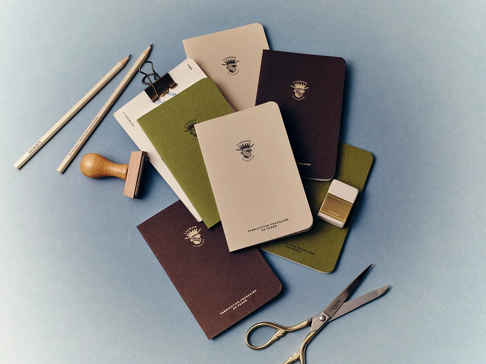 Carnets verts, beiges et marron, crayons et gomme Lignon sur un bureau bleu